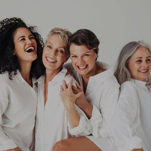Four happy women wearing white and embracing one another