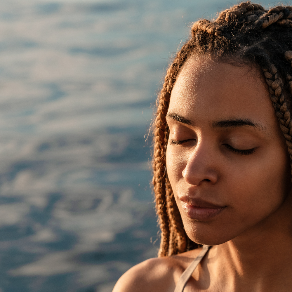 Woman next to water, eyes closed and sun on her face.