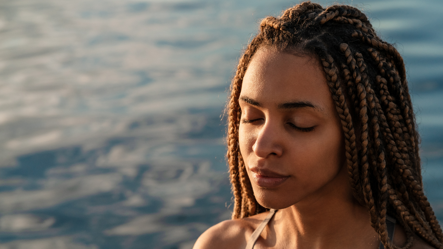 Woman next to water, eyes closed and sun on her face.